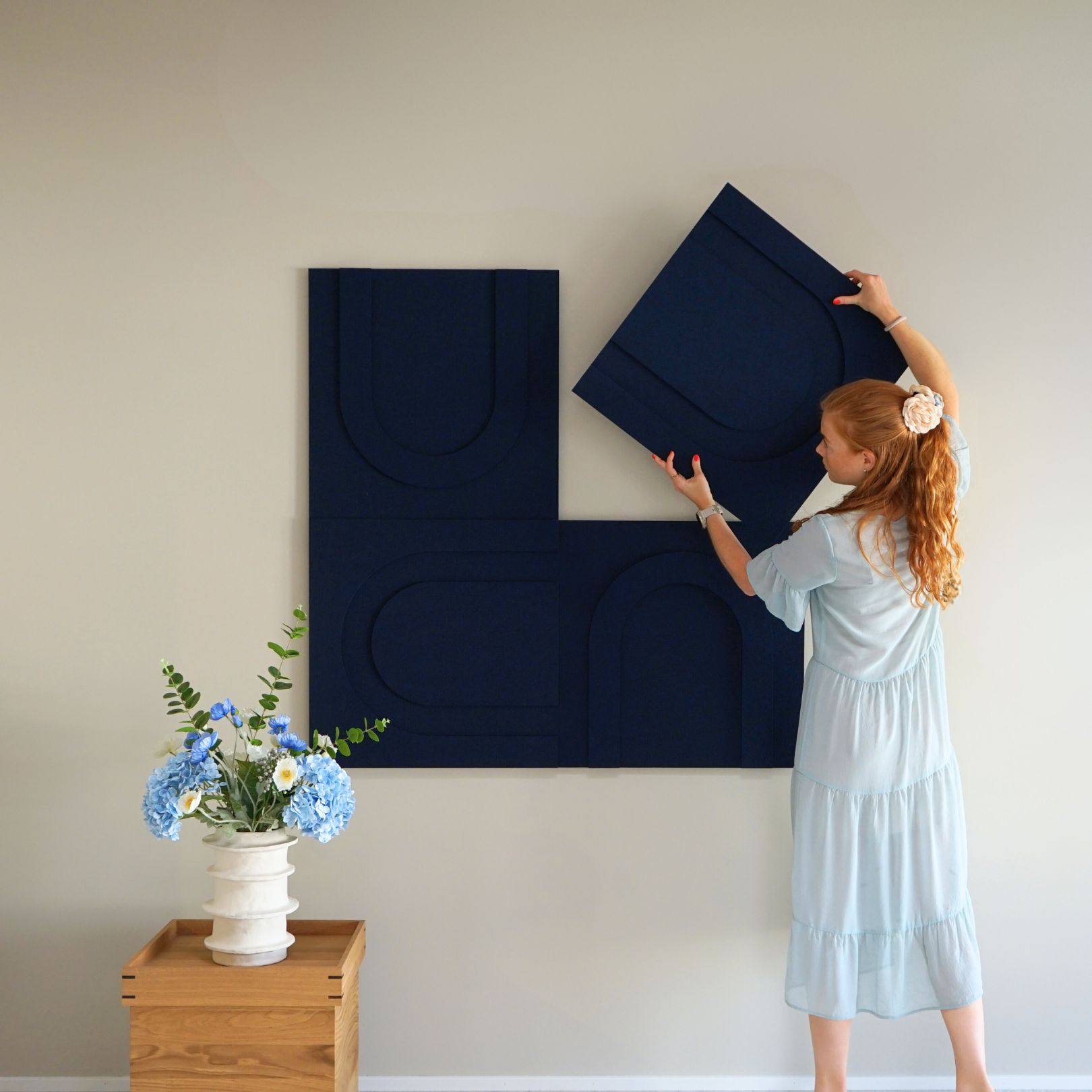 Woman installing blue geometric acoustic art panels from Arturel, designed for sound absorption and modern interior aesthetics.